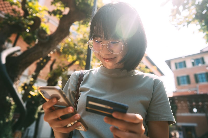 年轻的亚洲成年女性消费者使用信用卡和智能手机。