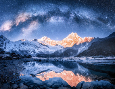 银河在雪山和湖的夜晚。景观上有白雪覆盖的高高的岩石，星空，倒影在尼泊尔的水中。天空的星星。喜马拉雅明