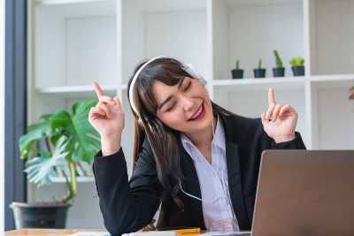 年轻的亚洲女性喜欢听音乐戴着耳机感觉放松的办公桌。
