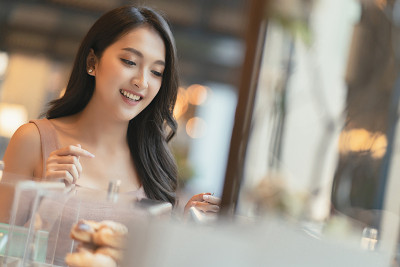 微笑的亚洲女性成年女性幸福愉快地选择精致的巧克力蛋糕和糖果在咖啡馆橱柜展示咖啡馆背景