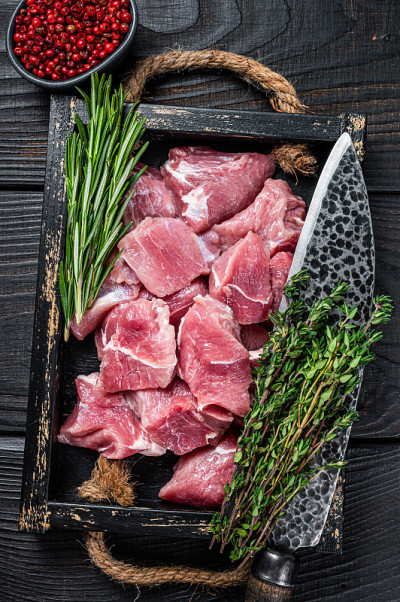 生切碎的猪肉幼崽肉与香料在一个质朴的托盘。黑色木制背景。俯视图