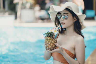 美丽的亚洲女人穿着比基尼在游泳池享受暑假。