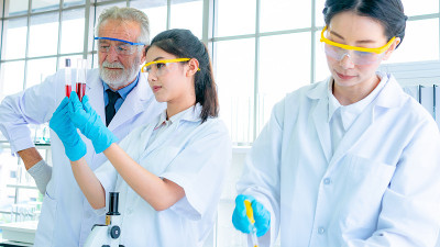 一队身穿白袍的教授、研究员、科学家，用桌上的科学设备配制试验化学液体。与浓度。与背景室内白色实验室。