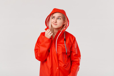 金发女孩穿着红色雨衣带着兜帽检查是否下雨开始孤立地站在白色的背景上。你准备好迎接寒冷的坏天气了吗?