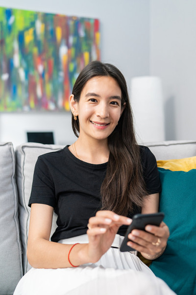 美丽的棕色头发和黑色眼睛的女孩在椅子上放松，手里拿着手机，浏览社交媒体，写短信，在屏幕上轻敲手指，对