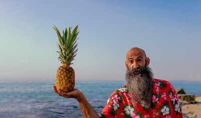 剃着光头，留着长胡子，穿着夏威夷衬衫，手里拿着一个菠萝