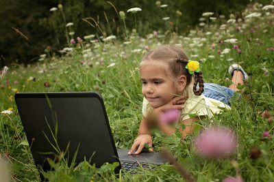 Pupil sitting on green grass outdoor and using lap