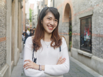美丽的年轻中国女子身穿白色毛衣和蓝色牛仔裤在上海新天地，微笑的石库门风格街道背景，快乐的时光，亚洲女
