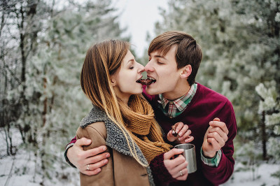 这是一对幸福的年轻夫妇在白雪覆盖的公园里吃圣诞饼干和姜饼的肖像。男人和女孩，喝着热红酒，热茶和咖啡。