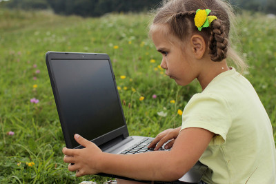 Pupil sitting on green grass outdoor and using lap