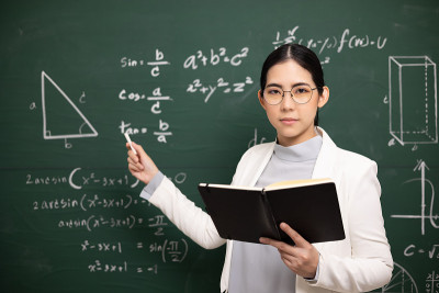 年轻的亚洲女教师手持书本和粉笔教学视频会议与学生看着摄像机。女教师从网络课程培训数学课堂黑板。