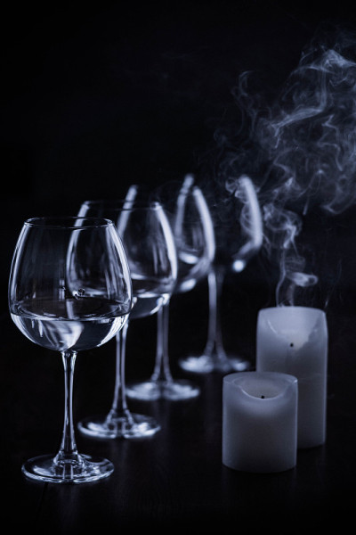 黑色背景下熄灭的蜡烛和玻璃酒杯。从蜡烛和餐桌上优雅的玻璃杯里冒出的烟。装有白葡萄酒的玻璃杯和蜡烛