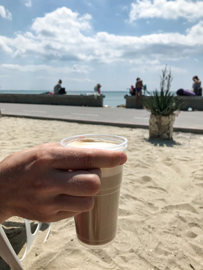 海滩上，一个女人的手拿着装在塑料杯里的卡布奇诺。Balchik。保加利亚。
