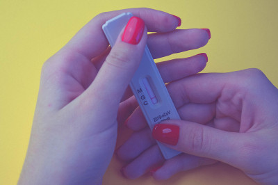 在橙色背景下进行冠状病毒测试。医学分析。修着鲜红色指甲的女孩正在做冠状病毒抗体测试，血液检测呈阴性