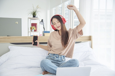 放松女人拿着书在床上用耳机听音乐。少妇放松阅读，翻开书本，休闲心灵。幸福美丽的女人人