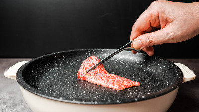 高级稀有切片牛腰和牛A5牛肉与高大理石纹理捡起和烧烤大理石涂层的不粘锅与手在黑色背景烧烤钳。对于日式