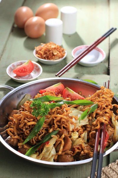 中式炒蛋面是一种传统的印尼食物，它将鸡肉、鸡蛋、西红柿、洋葱、蔬菜和甜酱油放在白色的木制餐桌上。