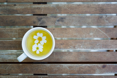木桌上放着茉莉花茶杯，上面放着几朵野雏菊