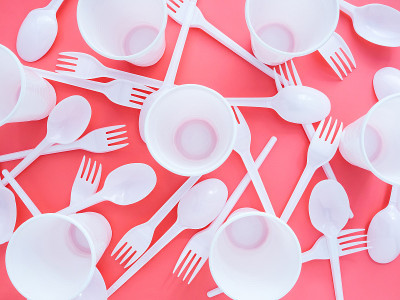 塑料白色的叉子、勺子和杯子分散在粉红色的背景上，平躺，俯视图。一个关于生态问题的明亮的现代概念。自然