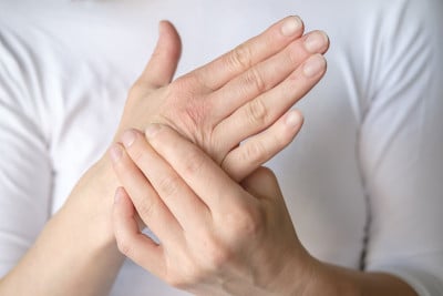 一名女子体验到手的疼痛，并在一件白色t恤上按摩一个痛点。