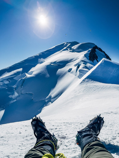 攀登勃朗峰(比安科山)山顶下4,808米雪坡的最后一步。男人的腿穿着带冰爪的靴子和登山服走过蓝色的天