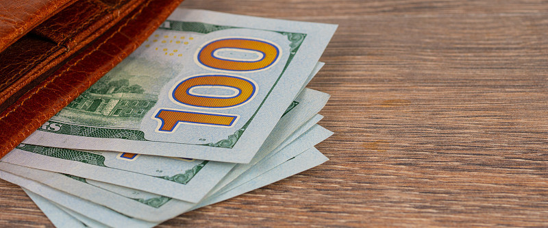 100美元钞票和橙色钱包放在木桌上。养老金或失业福利的概念。