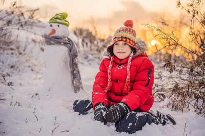 可爱的男孩穿着红色的冬衣堆雪人。冬季户外趣味概念