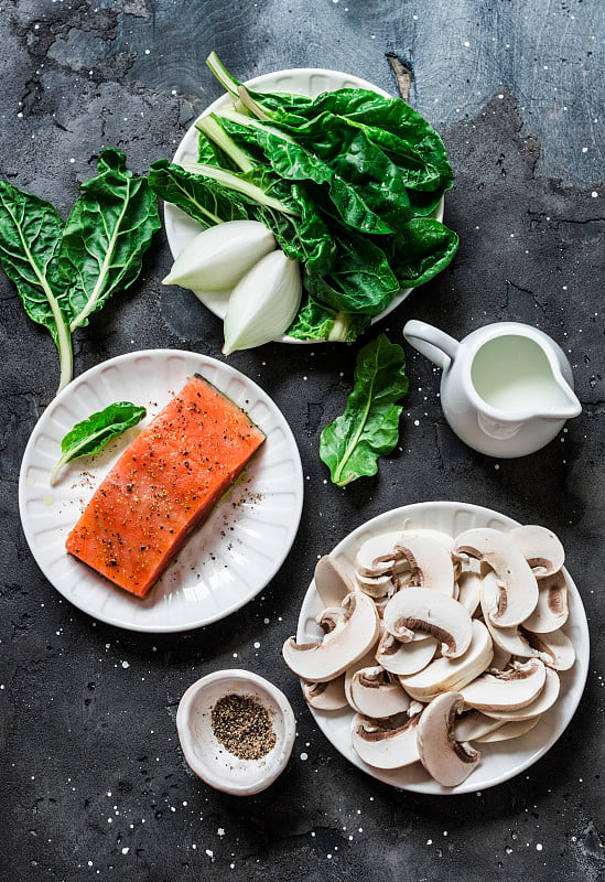 烹饪三文鱼的原料与奶油菠菜蘑菇酱在一个黑色的背景，俯视图。鲑鱼佛罗伦萨的午餐。菠菜、蘑菇和鲑鱼