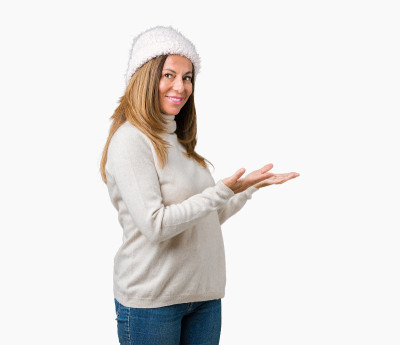 美丽的中年妇女穿着冬季毛衣和帽子在孤立的背景邀请进入微笑自然与开放的手