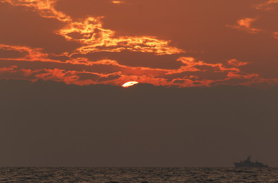 日落海滩背景。海浪在夕阳的余晖中。太阳落到地平线下。海平线上漂着一艘船
