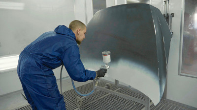 汽车油漆工在专用车棚的引擎盖上喷涂白色油漆