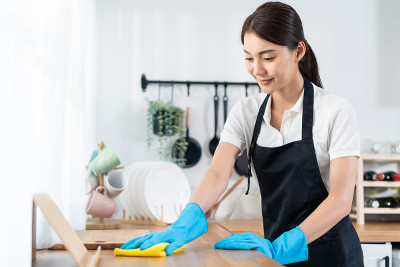 亚洲年轻清洁服务女工清洁厨房桌子在家里。美丽的年轻女孩管家清洁工感到高兴，并擦拭脏乱的烹饪柜台家务或