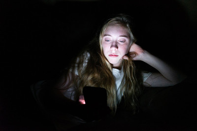 一个沮丧的女孩躺在黑暗中玩手机。