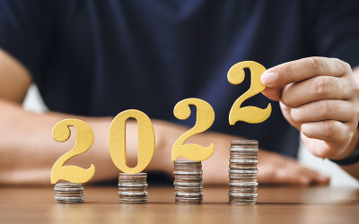 男子双手把黄金木制号码2022放在一叠硬币上。纳税、投资和银行概念。2022年新年省钱理财理念