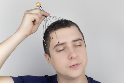 一个白色背景的男人用毛细管按摩器给自己做头部按摩。自助、抗压、放松理念
