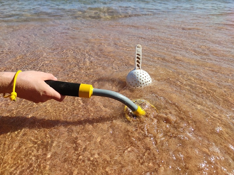 手拿水下金属探测器，用铲子在沙子上的照片。寻宝和旅游冒险背景。