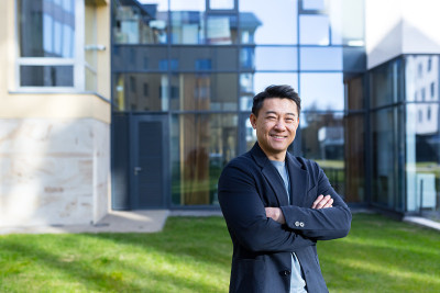 肖像英俊的亚洲人大学学院教师，商人，科学家或教育家。站在现代办公中心或校园背景，双臂交叉站在户外，对