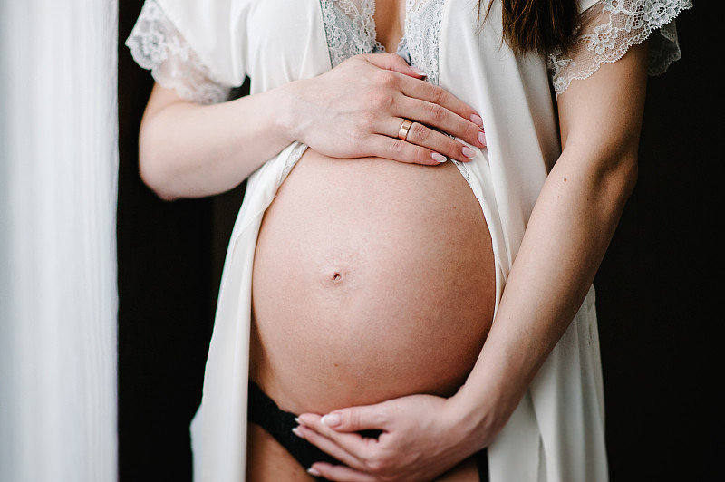 等待宝贝。孕妇站立时双手抱圆肚，腹部隆起。特写镜头。9个月。婴儿洗澡。母亲的概念。前视图。