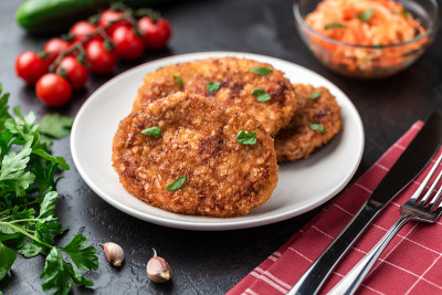 肉排躺在一个白色的盘子里。黑石桌上的青菜中间放着鸡排。