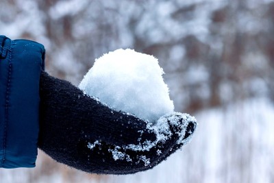 一个孩子戴着黑色手套的手拿着一团白雪。冬天的乐趣