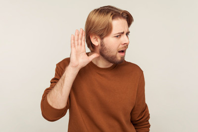 什么?我听不见!一幅穿着运动衫的大胡子男子的肖像，手放在耳边，听着耳语