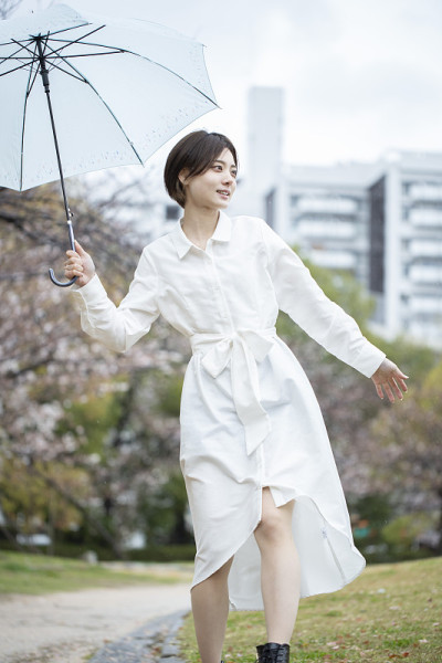 一个穿着白色连衣裙的年轻女子撑着伞在雨中行走