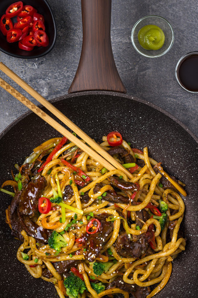乌冬炒面与牛肉和蔬菜在平底锅在黑暗的背景