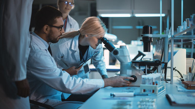 医学研究科学家团队致力于新一代疾病的治疗。他们用显微镜对培养皿中的样品进行分析。高级实验室生物技术研