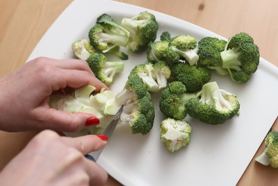 家庭主妇在白板上的木桌上切花椰菜