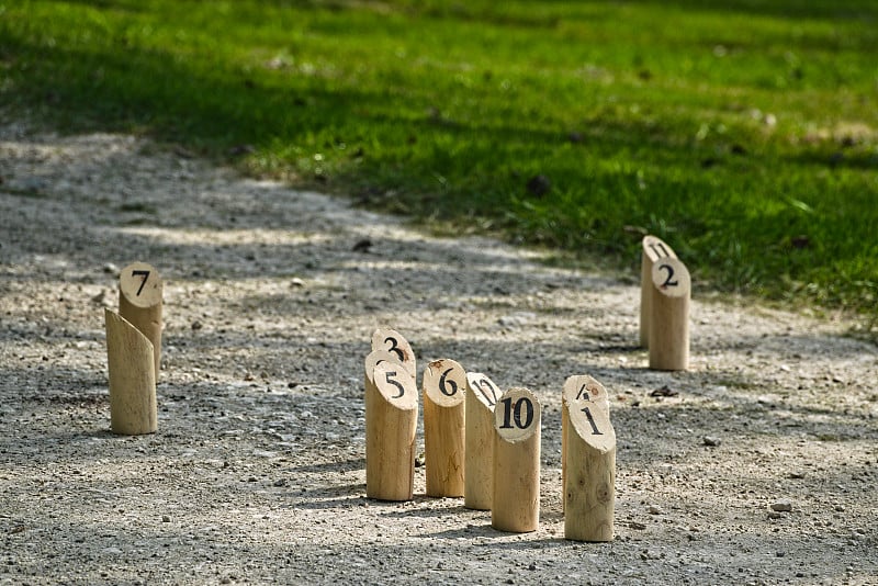 Mölkky的部分内容正在进行中，背景是放置在道路和草地上的保龄球瓶