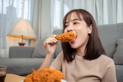 年轻的亚洲女性外卖吃垃圾食品鸡块鸡翅，女性享受安全的快餐外卖服务，并通过社交距离概念阻止冠状病毒的传