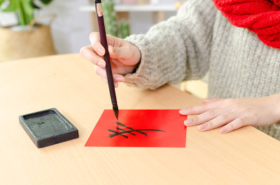 年轻的亚洲妇女用中国书法毛笔和砚台写春联。春节时在门上贴春联是中国文化的传统。
