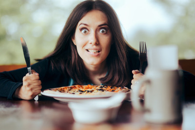 饥饿的女人拿着刀叉准备吃披萨