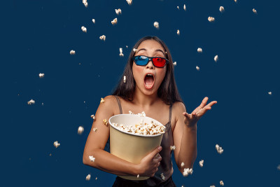 自由泳。年轻女子在3d眼镜孤立站在深蓝色扔爆米花一边嘴巴惊讶地张大
